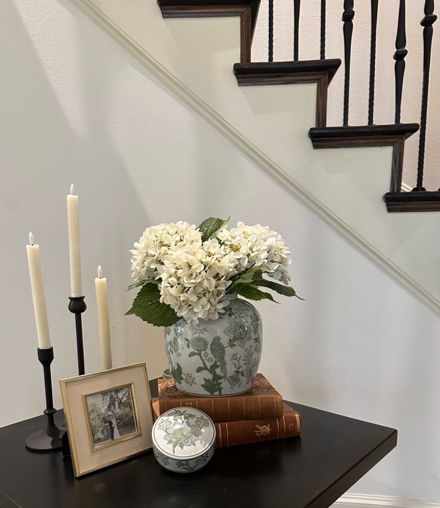 Vignette of a table styled with candles, a framed photograph, and vase with flowers