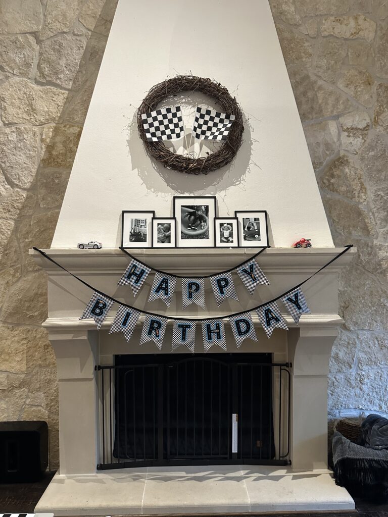Fireplace mantle with checkered flag wreath, black-and-white photos, and a Happy Birthday bunting.