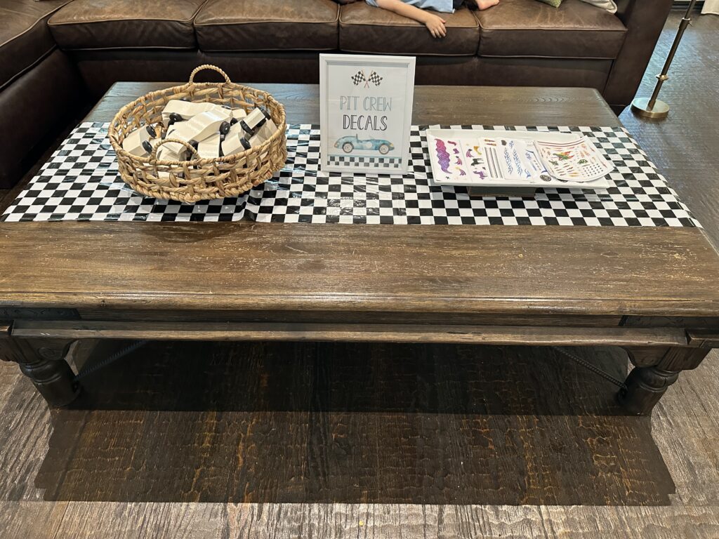 Coffee table with a basket of unpainted derby cars and sheets of decal stickers.
