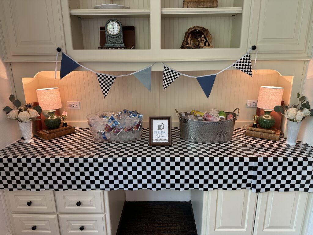 Checkered-tableclothed hutch with drink buckets, milk glass roses, and small trophies.]