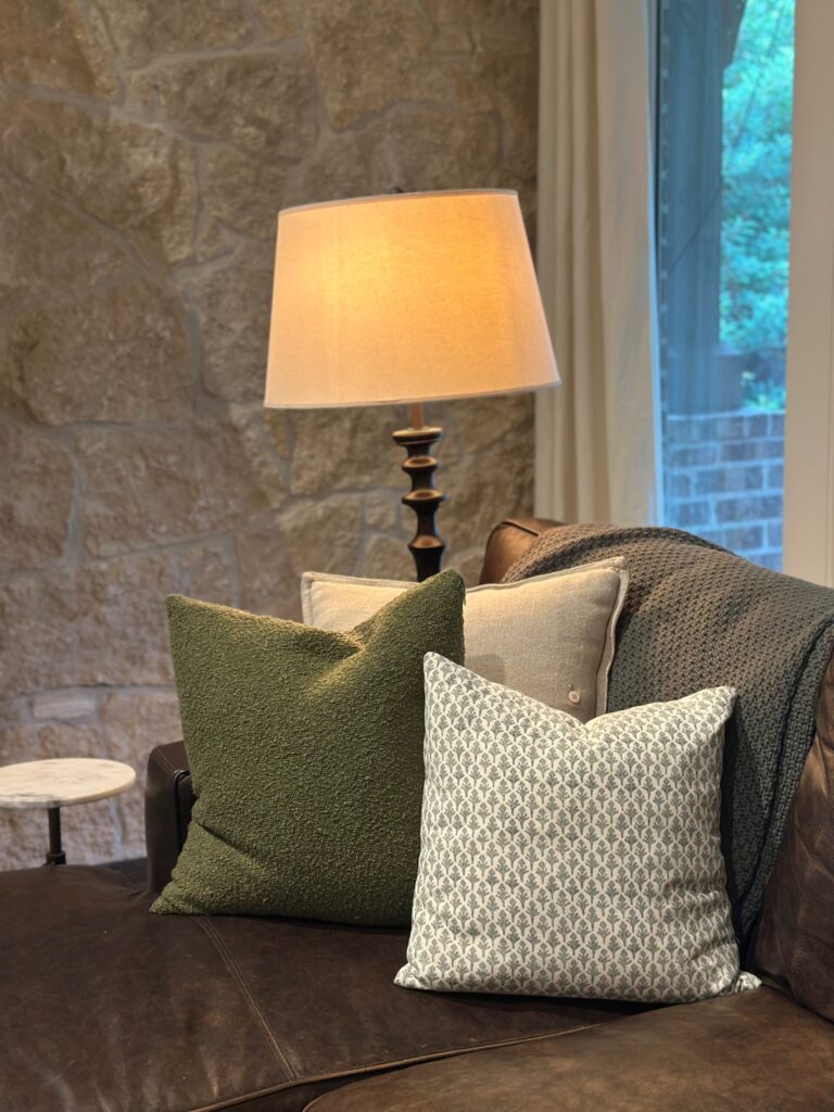 Leather sofa styled for fall with an olive throw pillow, block-print pillow, and chunky knit throw